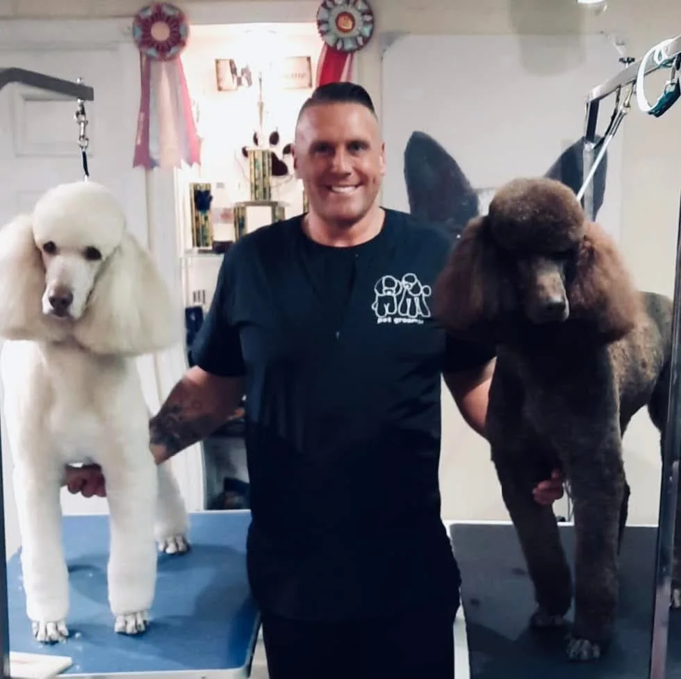 Dan standing with two poodles in a grooming setting